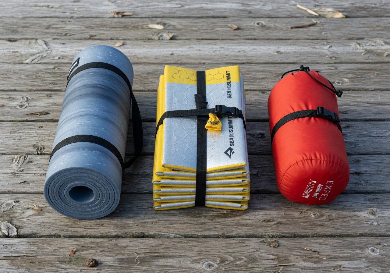 Three sleeping mat types side by side: rolled foam mat, Z-fold accordion pad, and inflatable sleeping pad in stuff sack